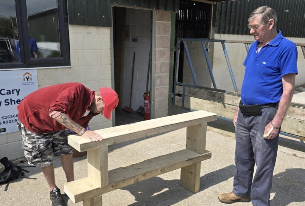 Photo of two men sanding a wooden bench.